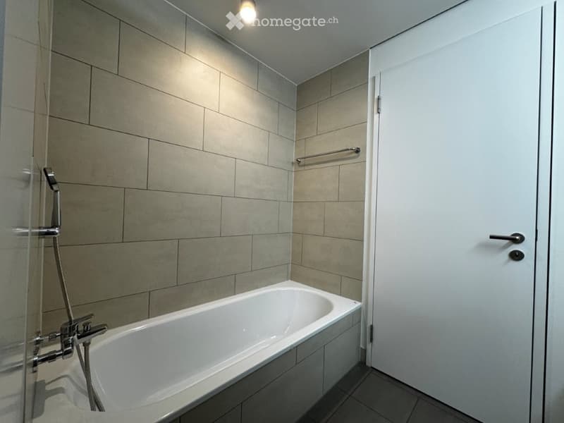 Modern bathroom with a white bathtub, glass shower enclosure, tiled walls, and a towel rack.