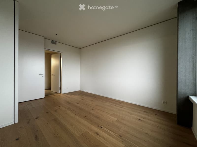 Empty room with light wooden flooring and white walls, featuring a doorway leading to another space.