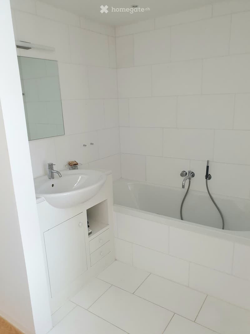 Modern bathroom with white tiles, a sink with a cabinet, a bathtub, and a mirror.