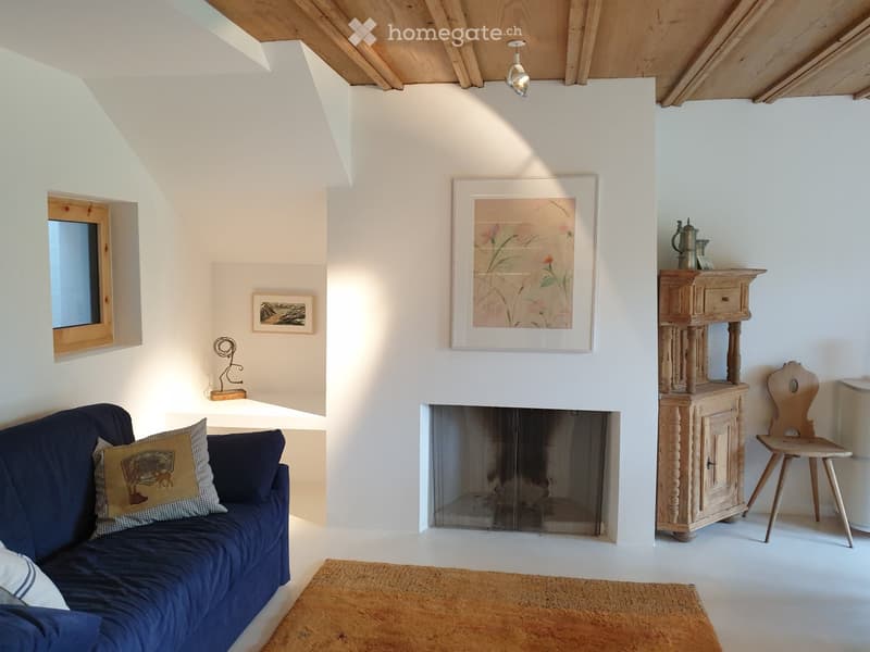 Living room with a blue sofa, fireplace, wooden table, chair, teapot, picture frames, and a sculpture on a shelf.