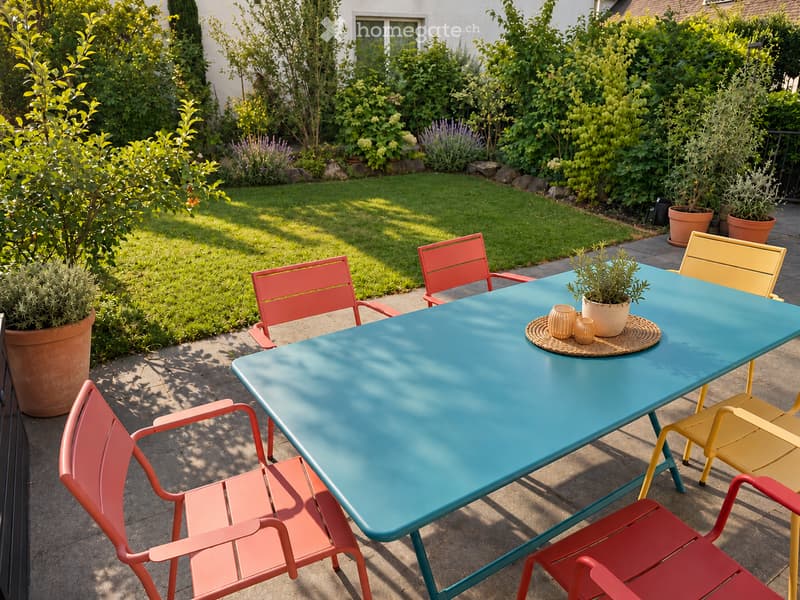 A sunny outdoor patio with a turquoise table, red and yellow chairs, potted plants, and decorative vases.