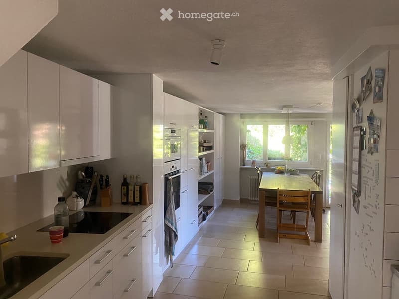 Modern kitchen with white cabinets, stainless steel appliances, a dining table with chairs, and various kitchen items on the counter and shelves.
