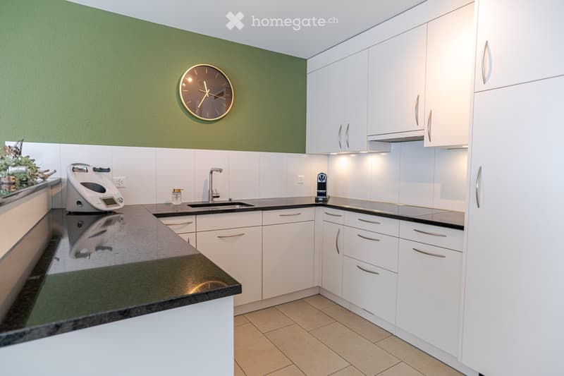 Modern kitchen with white cabinets, dark countertops, a sink, a coffee maker, a scale, and a clock on the wall.
