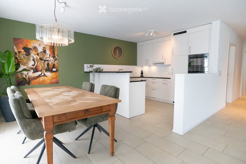 Open-plan dining and kitchen area with a wooden dining table, four chairs, white cabinets, a built-in oven, and a chandelier.