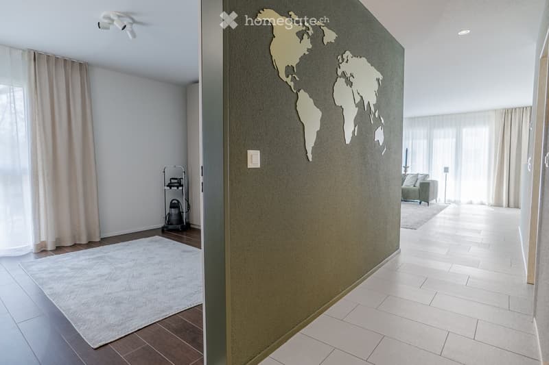 Modern hallway with a world map wall decoration, white tiled floor, and adjacent living room area with a sofa and large windows.