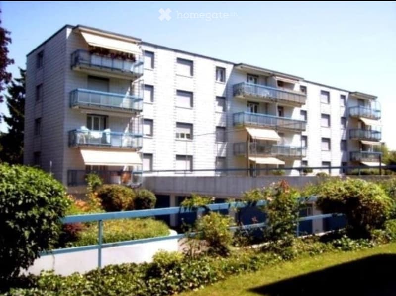 Modern multi-story apartment building with multiple balconies and a raised ground floor.