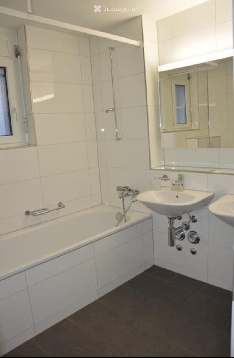 Modern bathroom with white tiled walls, a bathtub, a sink, and a large mirror above the sink.