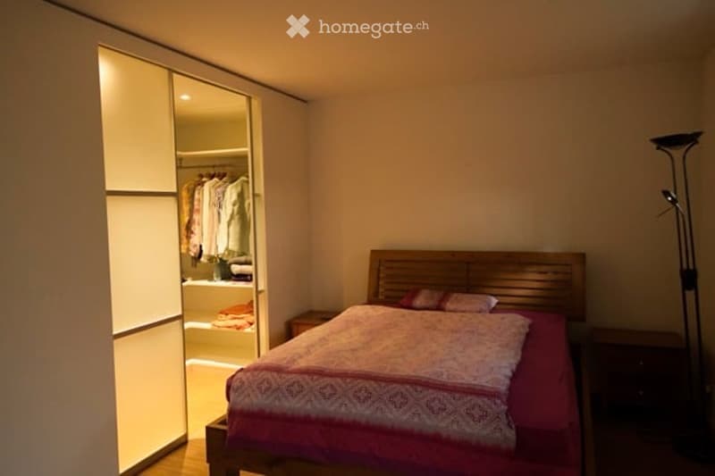 Cozy bedroom with a wooden bed, red bedding, nightstand, wardrobe, and floor lamp.