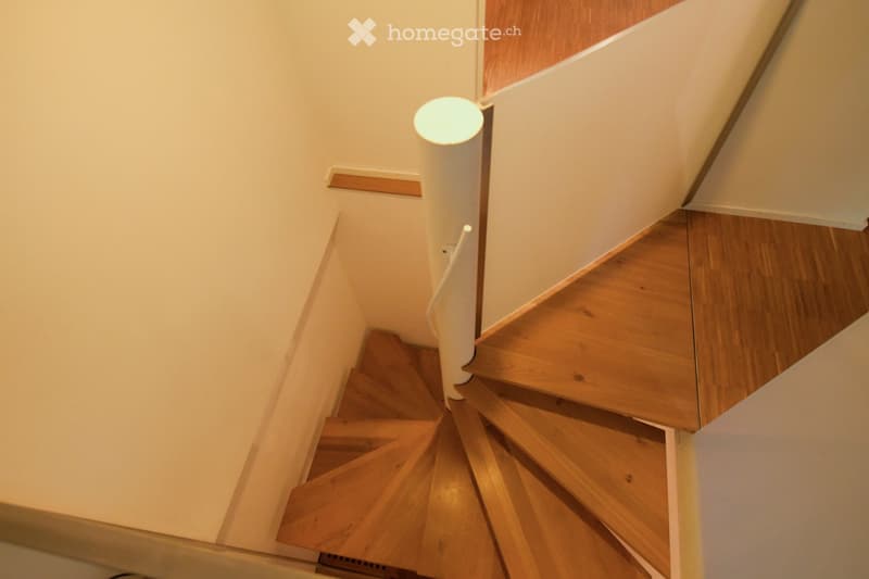 Wooden staircase with white railing and a single light fixture on the wall.