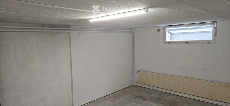 Empty room with concrete floor, white walls, fluorescent lighting, and a small window with blinds.