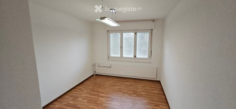 Empty room with wooden flooring, white walls, a window with blinds, and a radiator below the window.