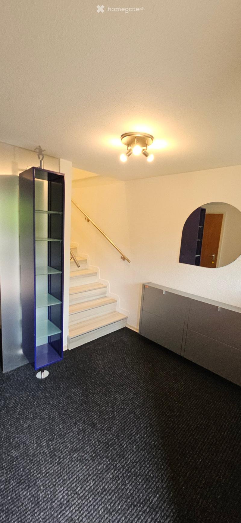Hallway with carpeted floor, staircase leading upwards, glass display cabinet, built-in storage unit, and a mirror on the wall.