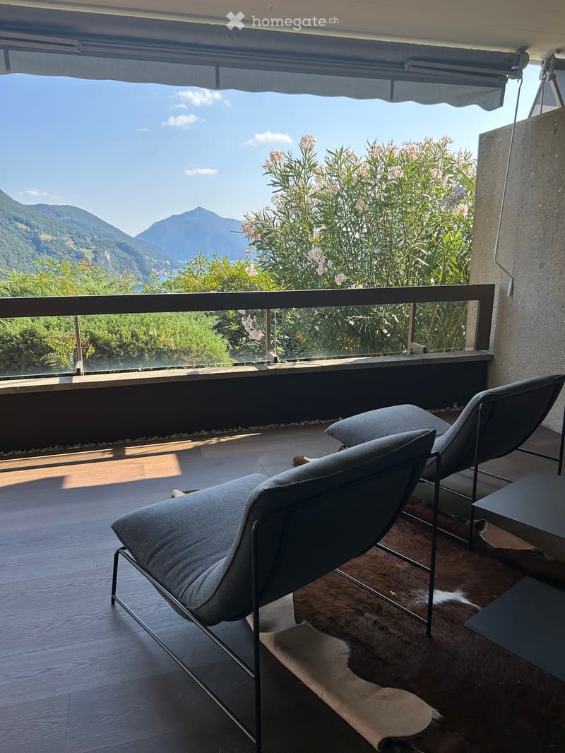 Balcony with wooden flooring, two modern chairs, a small table, and a fur rug, overlooking a scenic mountain view.