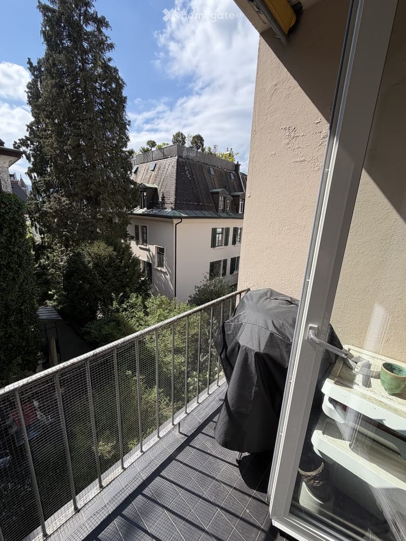 Balcony with metal railing, tiled floor, and a view of a neighboring building and trees.