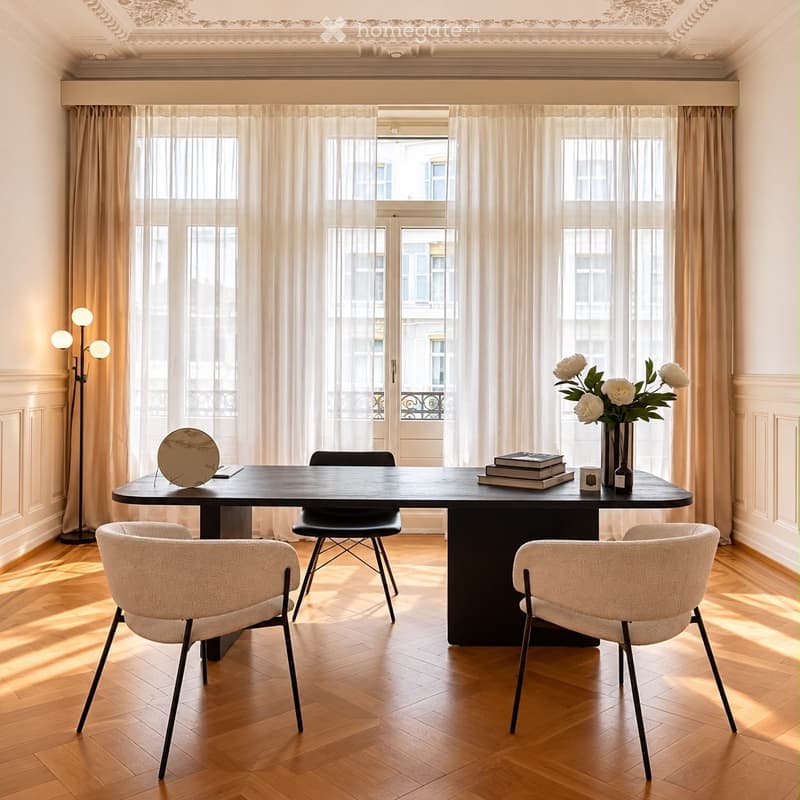 Elegant dining area with a dark wooden table, four modern chairs, a vase with white flowers, books, and a decorative plate on the table. Natural light streams in through large windows with sheer curtains, complemented by a floor lamp.