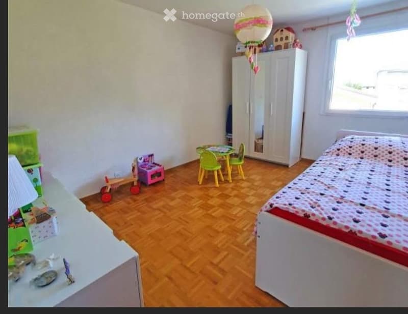 A child’s bedroom with a bed, wardrobe, small table and chairs, and various toys including a toy house and a balloon decoration.