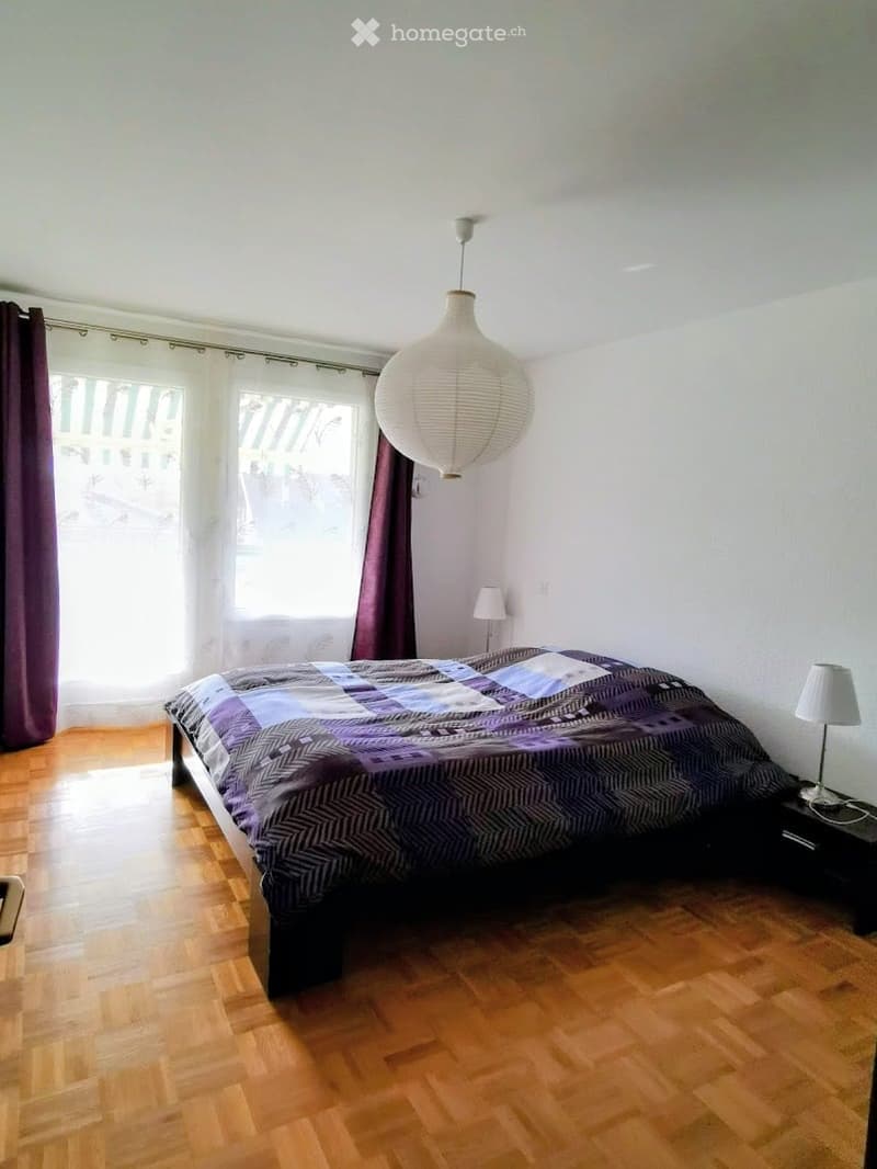 Cozy bedroom with wooden flooring, a large bed with a patterned duvet, a hanging paper lantern, and two bedside lamps.