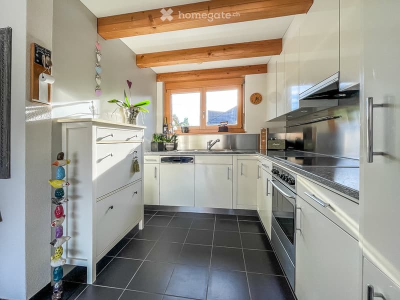 Modern kitchen with white cabinets, stainless steel appliances, dark tiled floor, and a window above the sink.