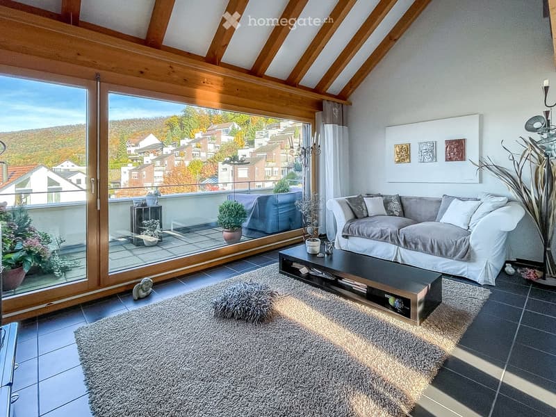 Modern living room with a large window offering a scenic view, featuring a grey sofa, coffee table, plush rug, and decorative candle holder.