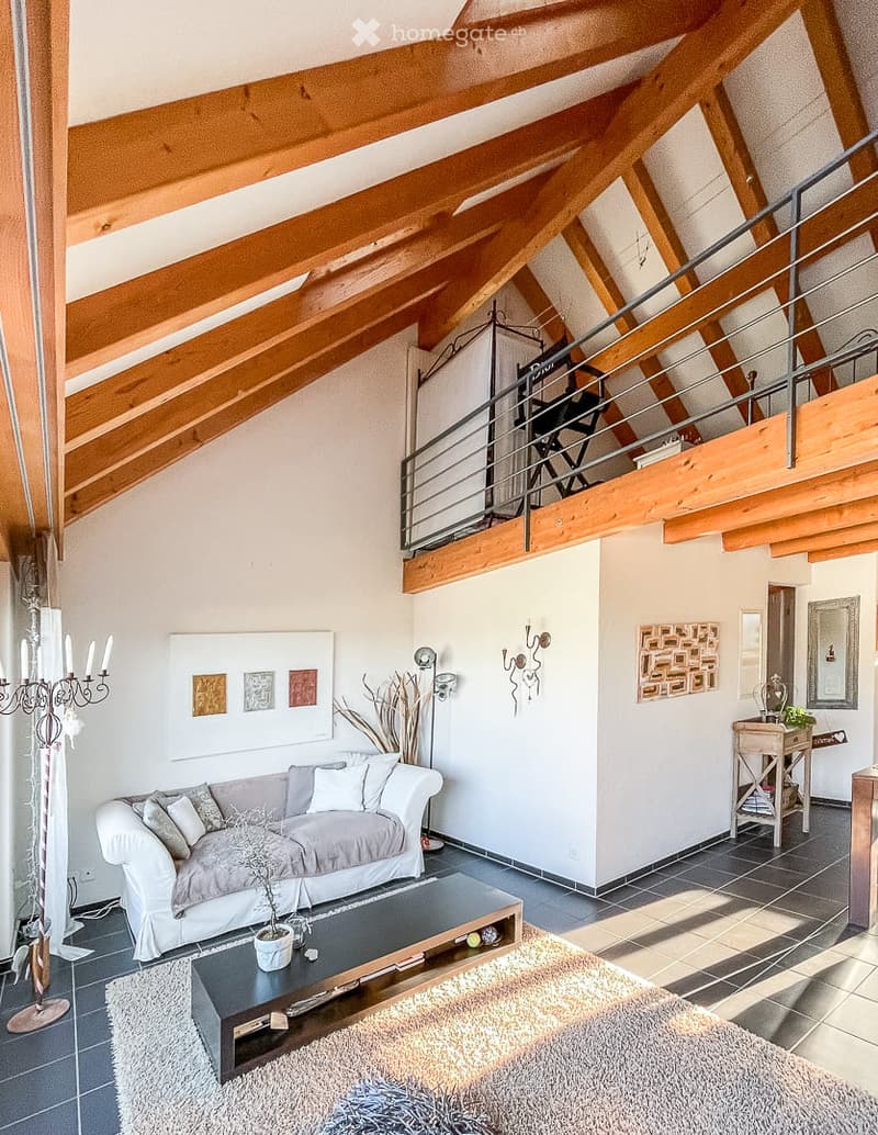 Bright living room with exposed wooden beams, a grey sofa, coffee table, floor lamp, side table, and decorative wall art.