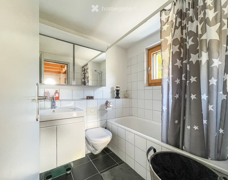 Modern bathroom with white tiles, a bathtub, toilet, sink, and a large mirror above the sink. The shower area is enclosed with a dark curtain featuring a star pattern.