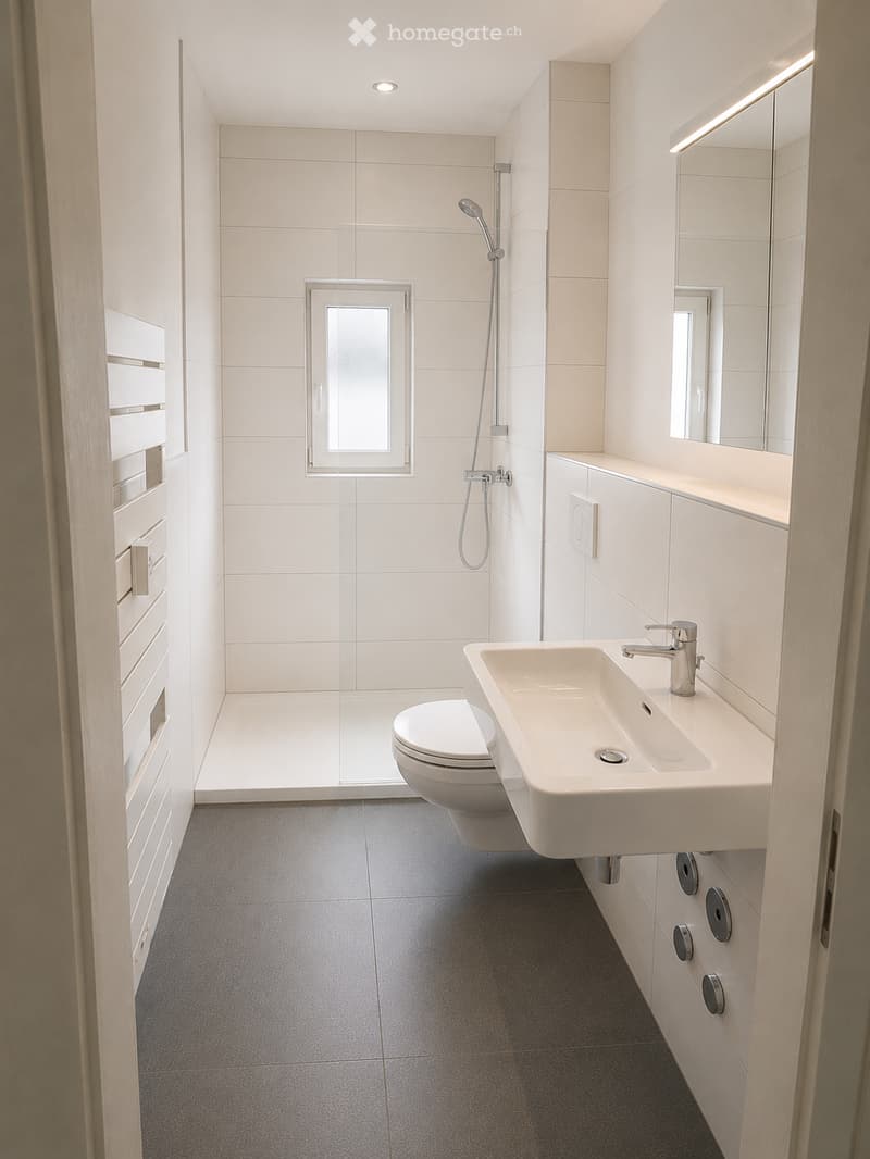 Modern bathroom with white tiles, a toilet, a sink with a modern faucet, a large mirror, and a shower area with a glass enclosure.