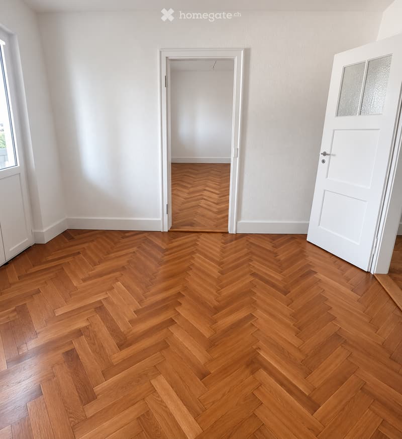 Empty room with herringbone-patterned wooden flooring, white walls, and white doors.