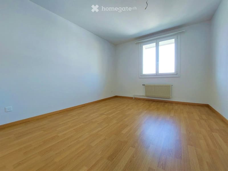 Empty room with wooden flooring, white walls, and a window with white frame. A radiator is visible below the window.