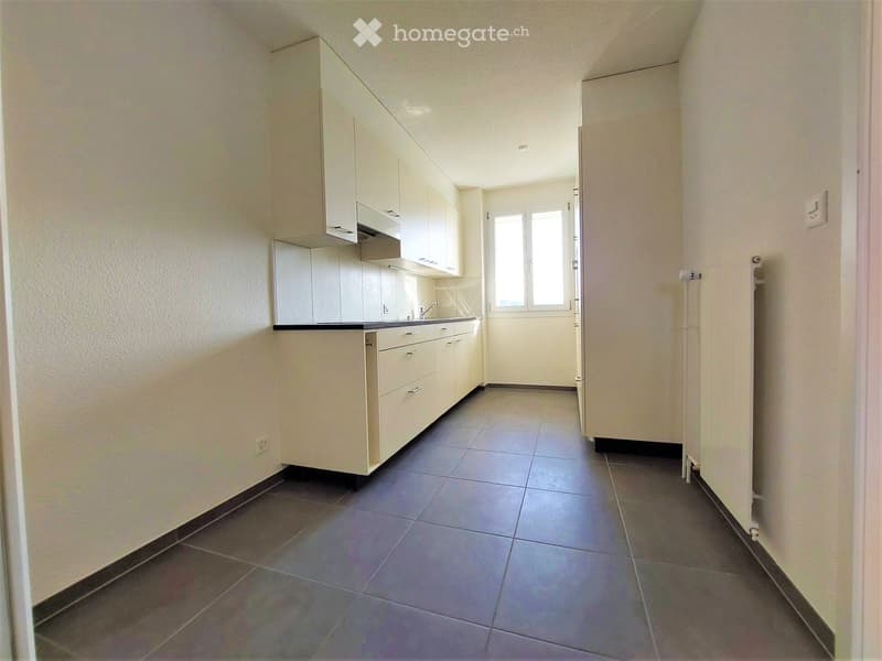 Modern kitchen with white cabinets, dark tiled floor, and a window at the end of the space.