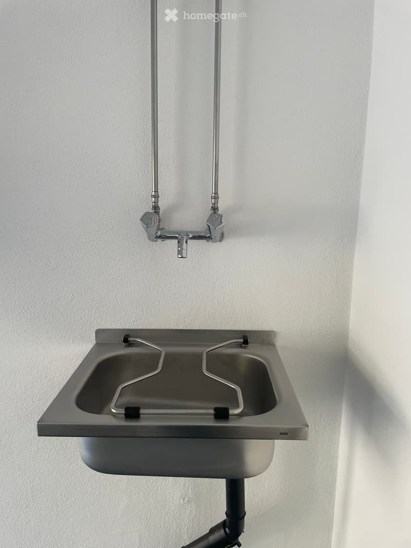 Stainless steel sink with dual faucets mounted on a white wall.
