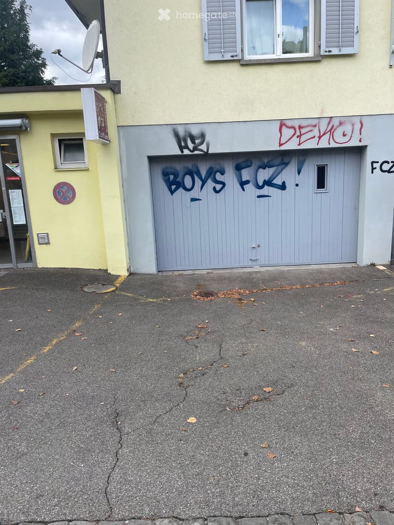 Two-story building with graffiti on the garage door and a satellite dish on the roof.