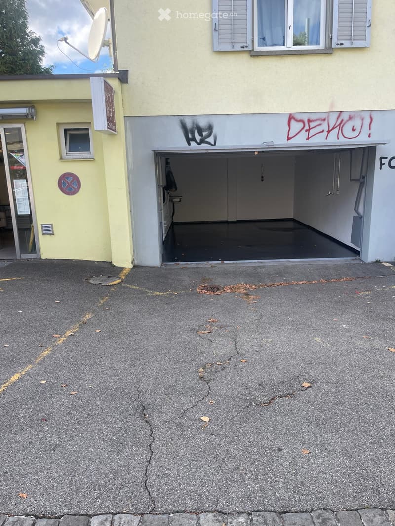 Building exterior with a garage entrance, graffiti on the facade, and a satellite dish on the roof.