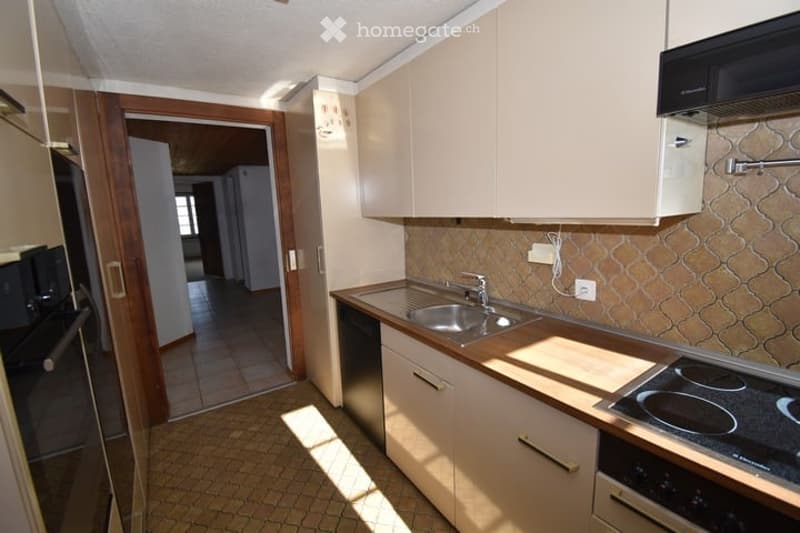 Modern kitchen with light-colored cabinets, a stainless steel sink, and a stove. The floor is tiled, and there is a doorway leading to another room.