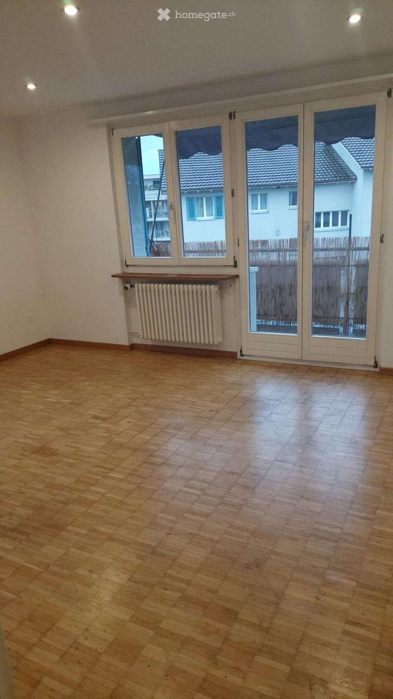 Empty room with wooden flooring, large windows, radiator, and sliding glass doors leading to an outdoor area.
