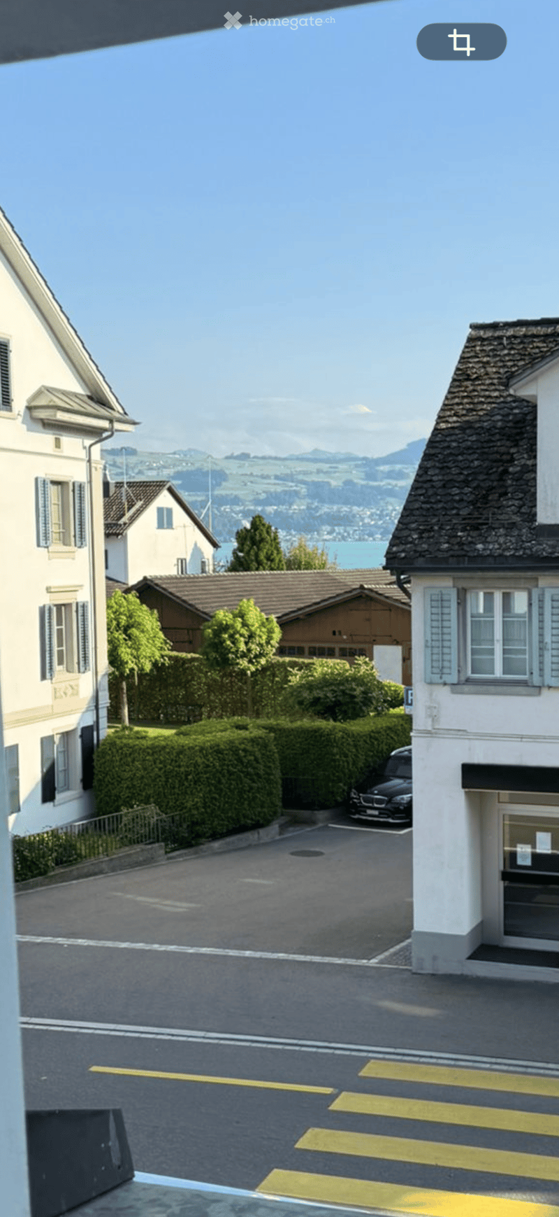 Residential street with multiple houses, parked car, and scenic mountain view in the background.