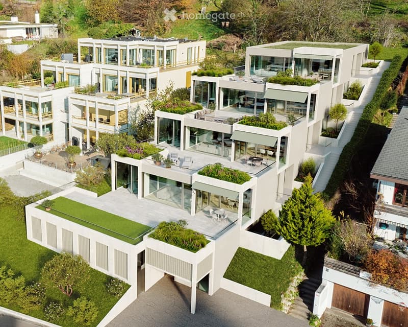 Aerial view of a modern, multi-level white residential complex with large glass windows, green rooftop gardens, and outdoor seating areas.