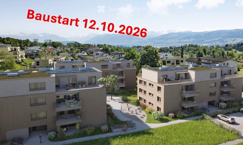 Aerial view of a modern residential complex with multiple apartment buildings, balconies, green spaces, and surrounding landscape with mountains in the background.