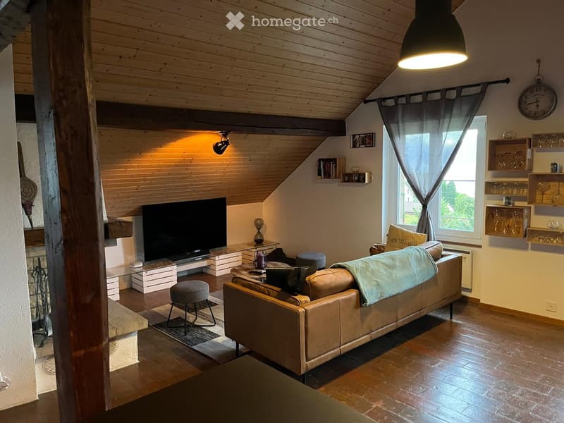 Cozy living room with wooden ceiling beams, exposed wooden walls, and warm lighting. Features a large leather sofa, coffee table, TV, and decorative shelves.