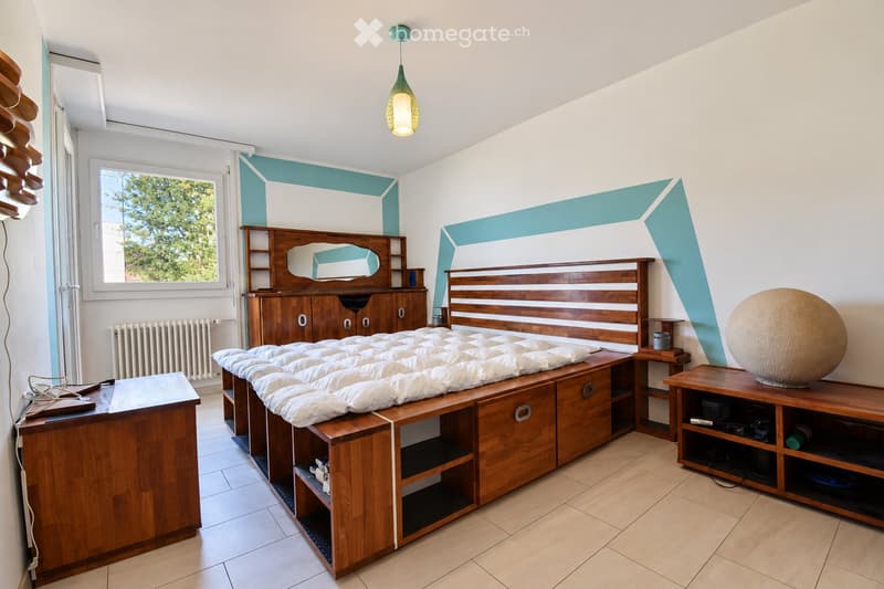 A well-lit bedroom with a wooden bed, a large mirror, a wardrobe, a nightstand, and a decorative ball on a table.
