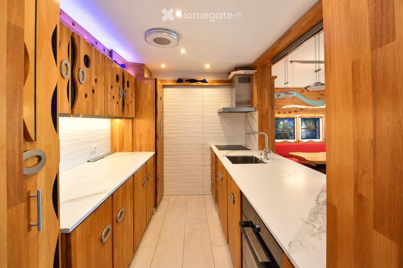 Modern kitchen with wooden cabinets, white countertops, stainless steel sink, and built-in oven. Features pendant lighting and a sleek design.