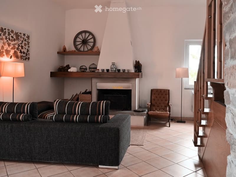 {"visible_features": ["Fireplace"],"type": "Living room","description": "Large living room with a dark gray sectional sofa, a tufted leather armchair, a fireplace with a wooden mantel, and shelves displaying decorative items. The room has tile flooring an