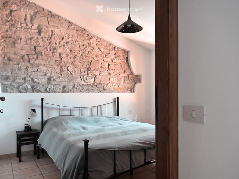 Bedroom with exposed brick wall, black metal bed frame, bedside table, and pendant light fixture