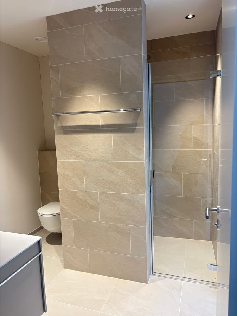Modern bathroom with beige tiled walls and floor, a glass-enclosed shower, a toilet, and a modern faucet.