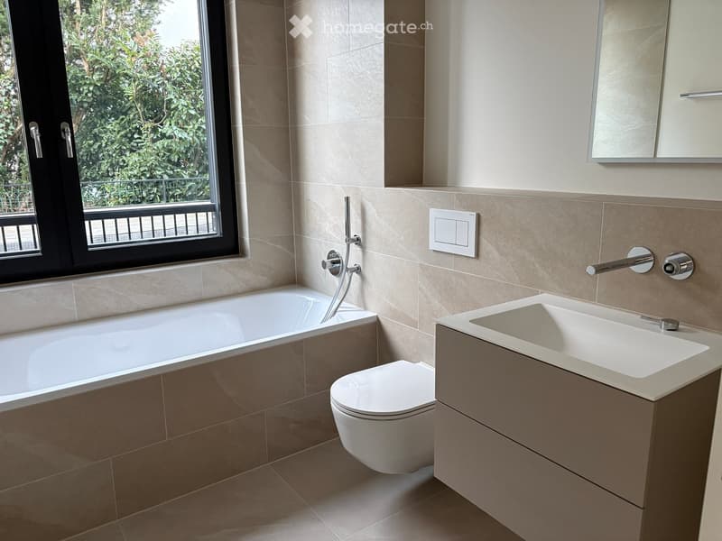 Modern bathroom with a bathtub, toilet, sink, and large window offering a view of greenery outside.