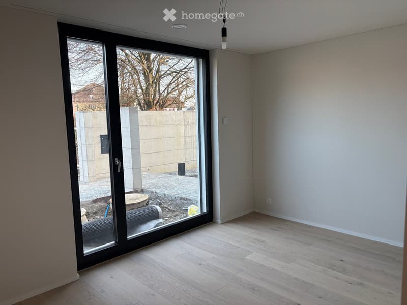 Empty room with light wooden flooring, white walls, and large sliding glass doors leading to an outdoor area.