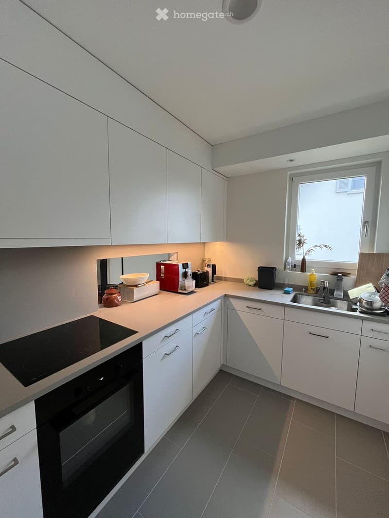 Modern kitchen with white cabinets, induction stove, oven, sink, and various appliances on the counter.