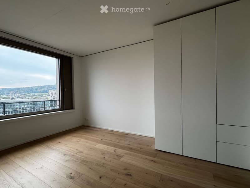 Empty room with wooden flooring, white walls, large window with a view, and built-in closet.