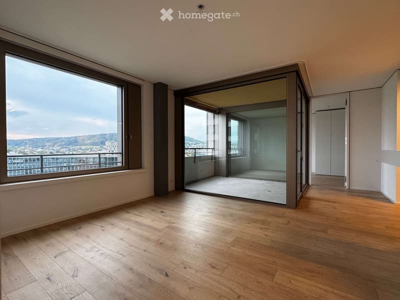 Empty room with wooden flooring, large windows, and a sliding glass door leading to a balcony with a scenic city view.