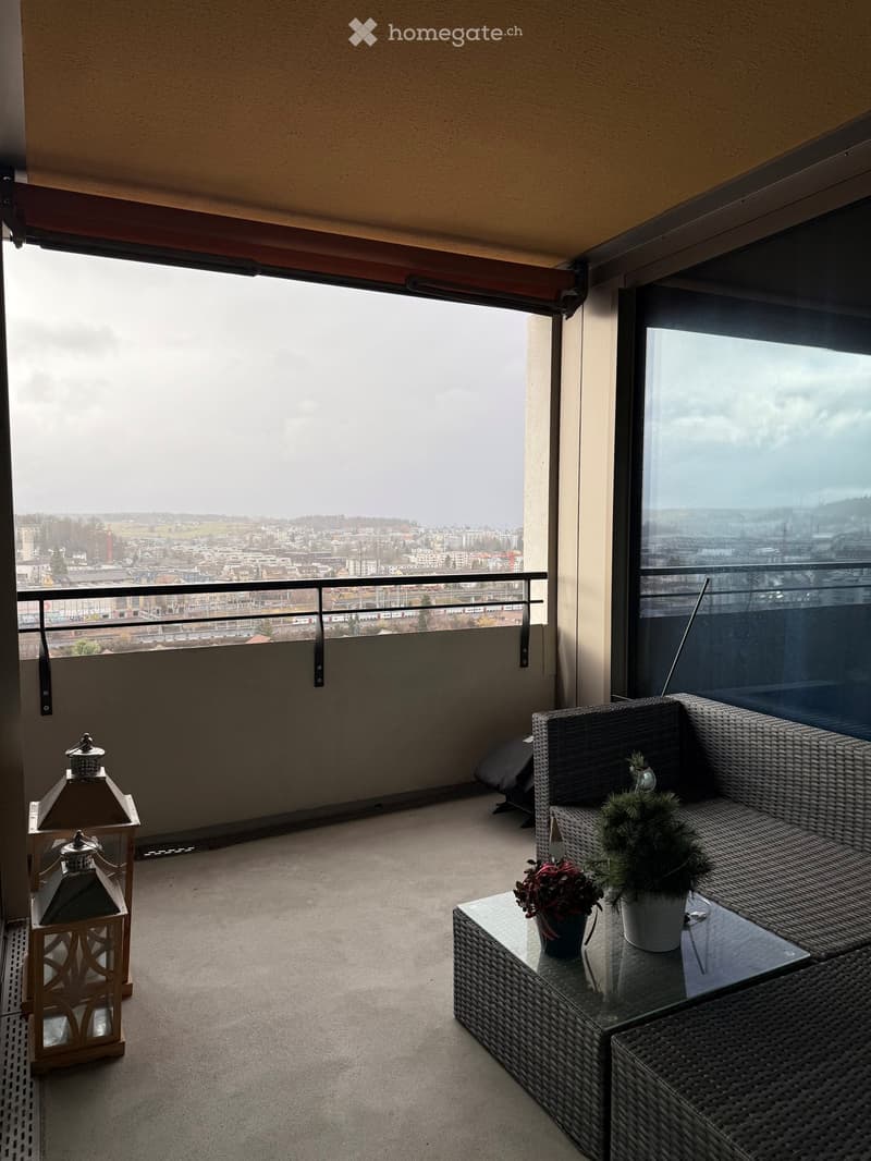 Balcony with railing, couch, table, plants, lanterns, city view