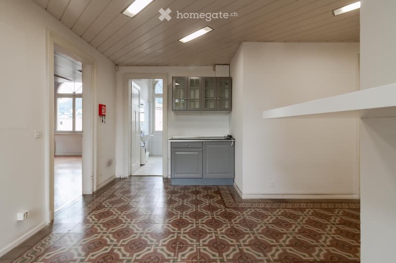 Empty room with white walls, patterned tile floor, grey cabinets, and a sink visible in the adjacent space.